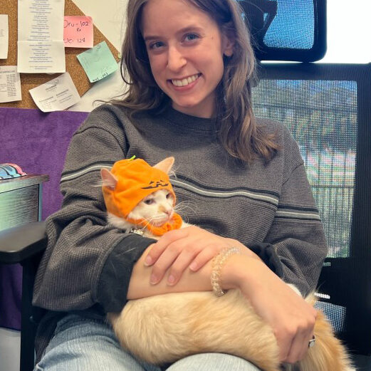 A cat wearing a funny hat being held by Kaylee at Paz East Austin